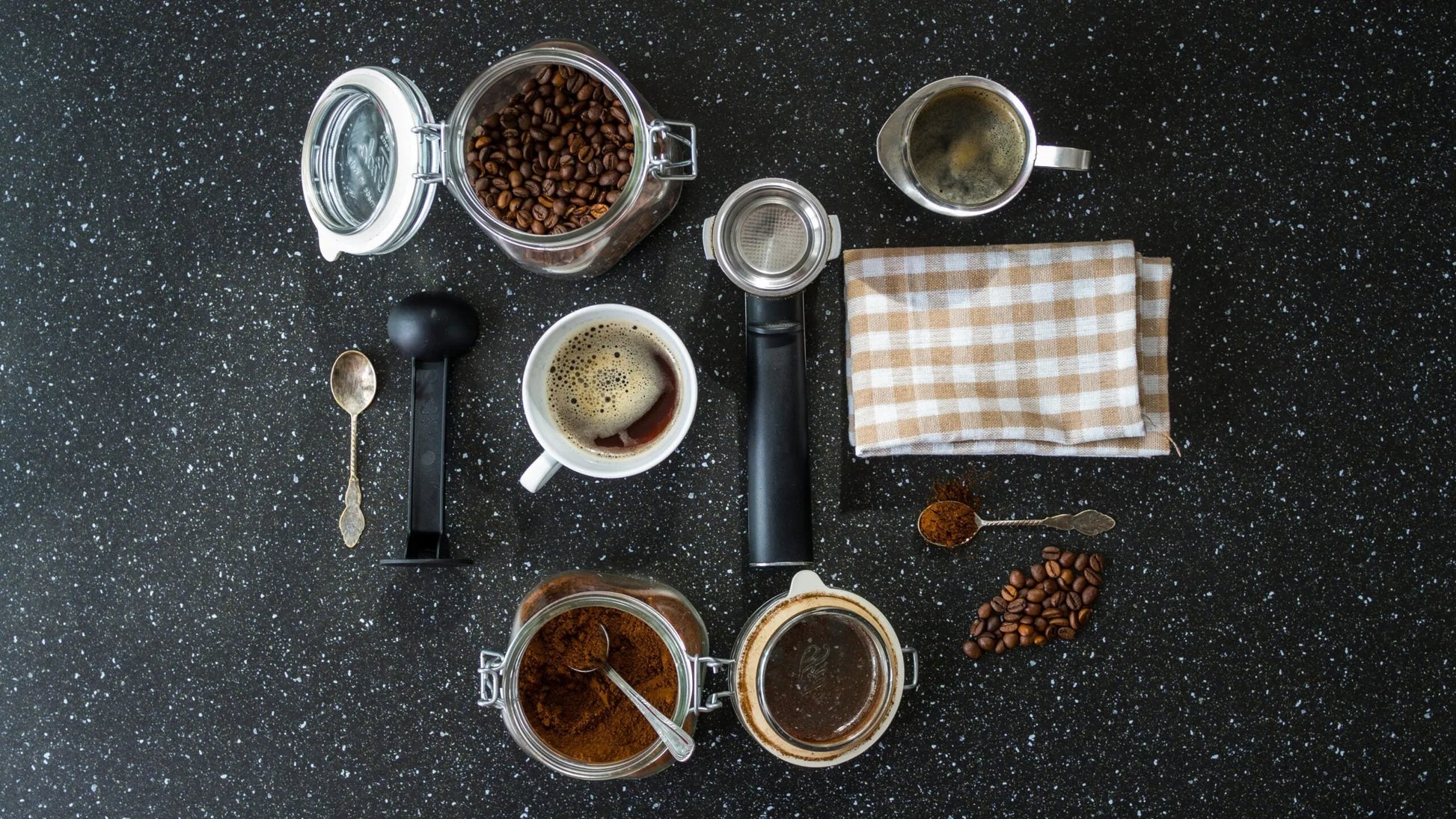 Top view of coffee brewing setup with beans, cup, and accessories on black granite.